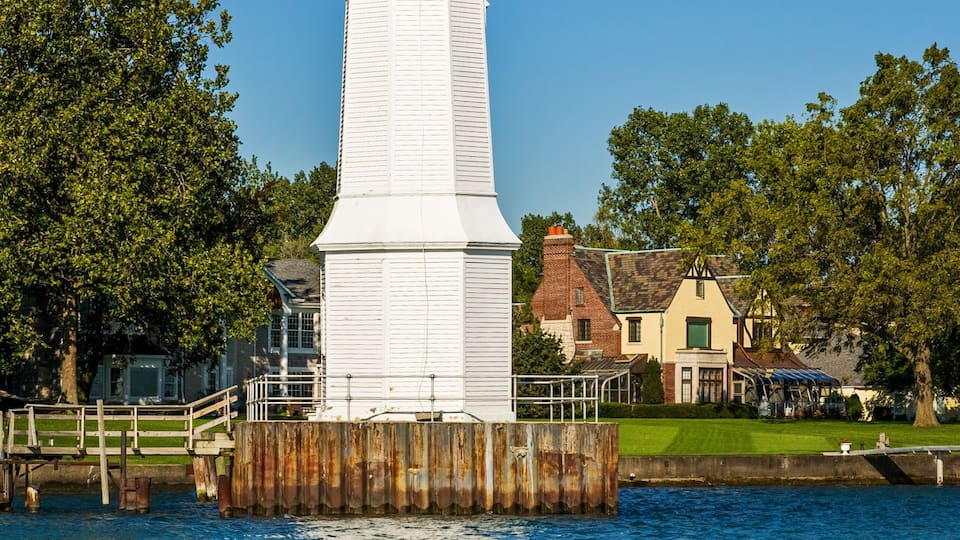 A white lighthouse on a wooden pier with a clear blue sky and a visible moon.