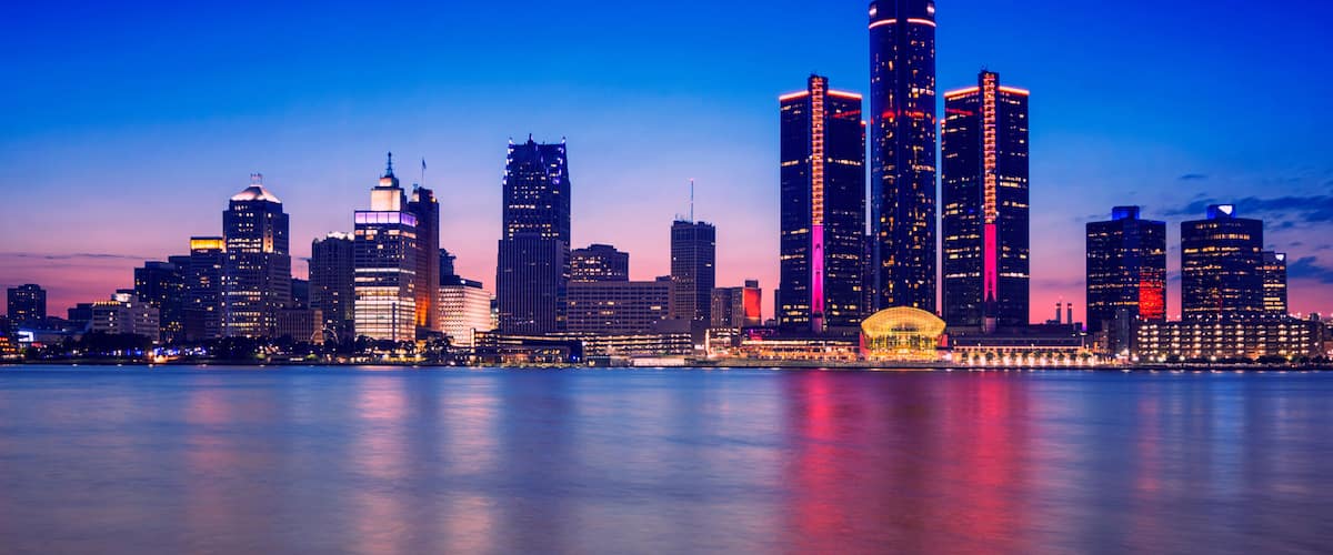 A city skyline at dusk with illuminated buildings reflecting on the water.