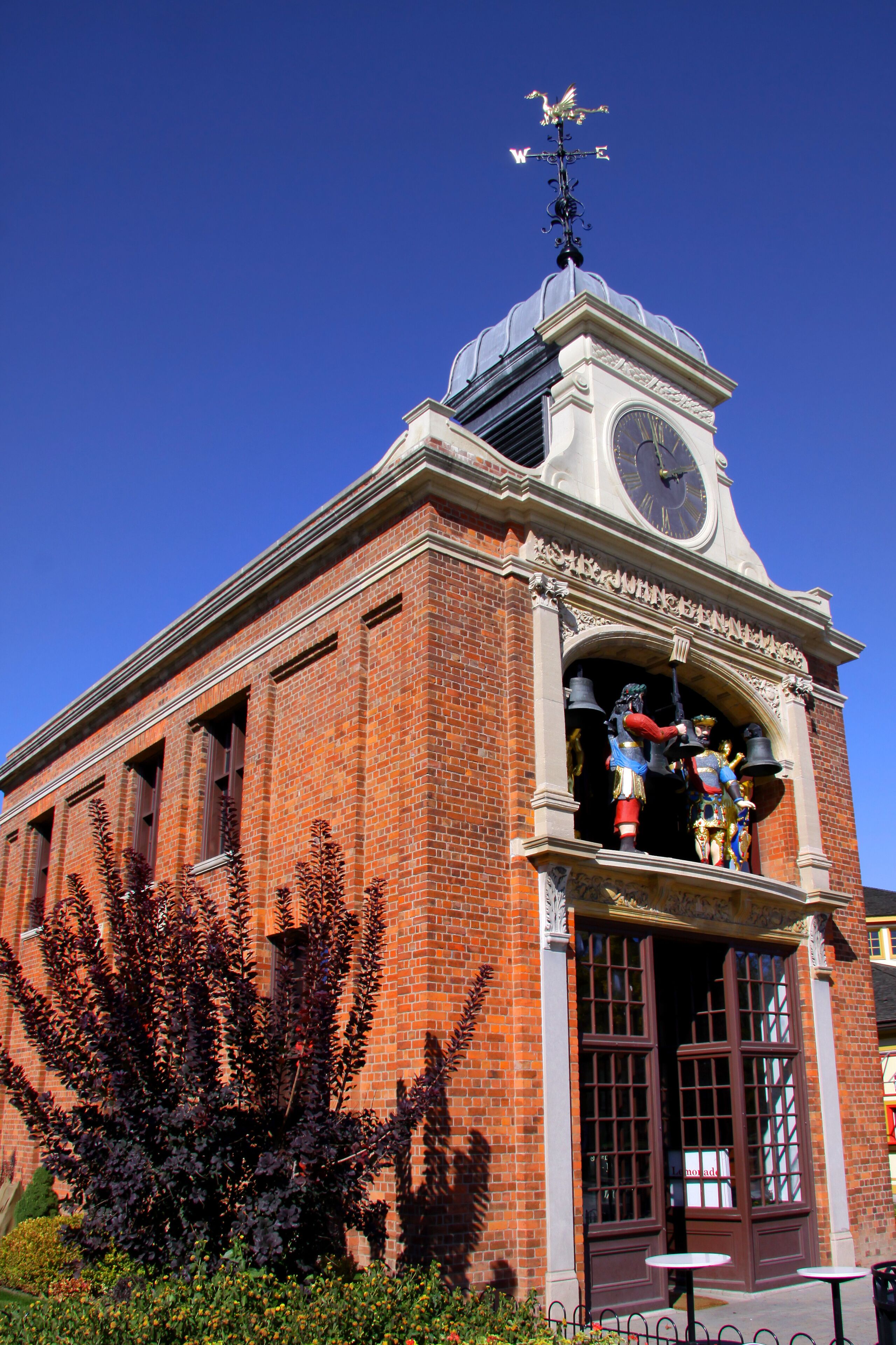 A brick building with a clock tower, a weather vane, and a statue of a man with a flag.