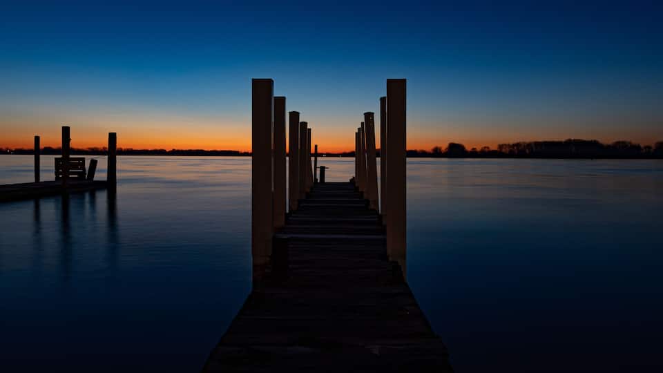 A wooden pier extending into calm water at dusk with a clear sky.