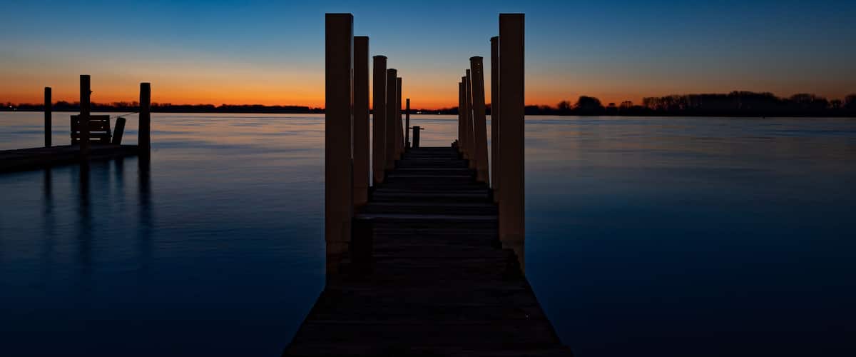 A wooden pier extending into calm water at dusk with a clear sky.