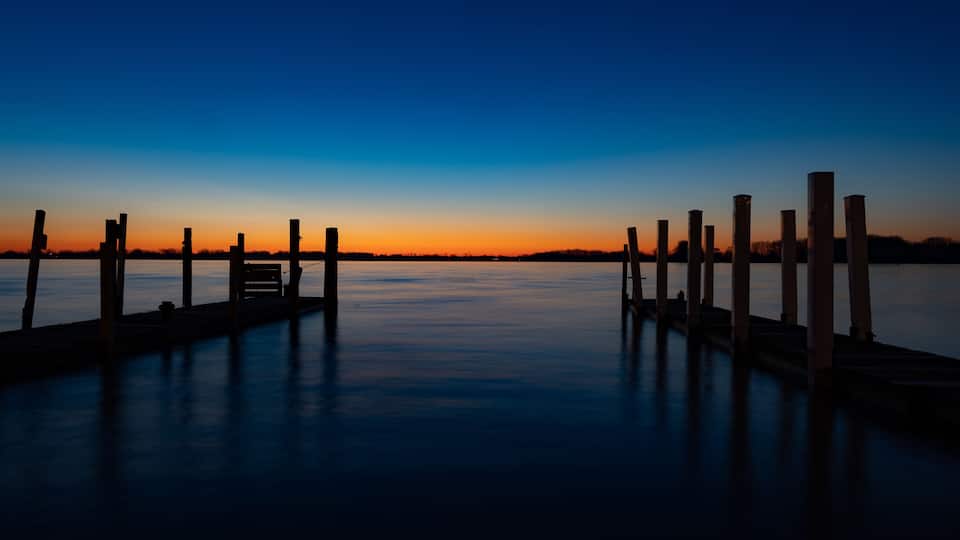 A pier extending into calm water at sunset with a clear sky.
