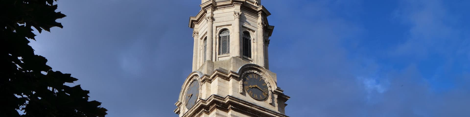 A classical building with a prominent clock tower, columns, and a clear blue sky.