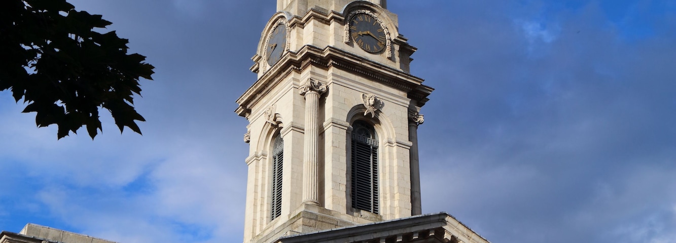 Ein klassizistisches Gebäude mit einem markanten Glockenturm, Säulen und einem strahlend blauen Himmel.