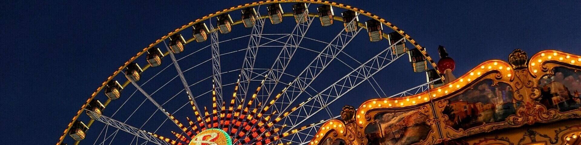 A Ferris wheel with a large illuminated 'B' at the center and a carousel with ornate decorations.