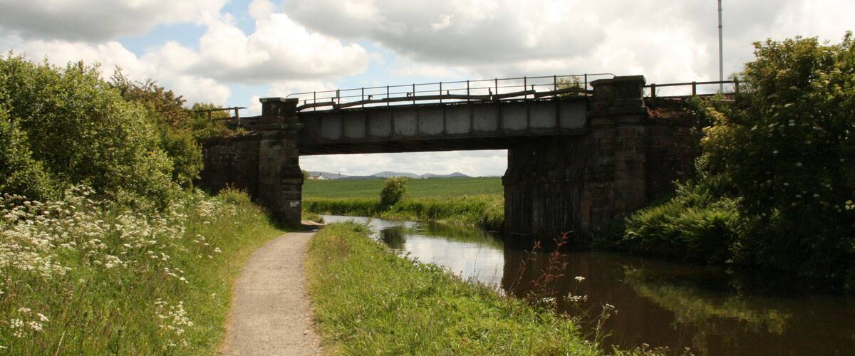 Un puente de piedra sobre un canal estrecho, rodeado de vegetación y un cielo despejado.