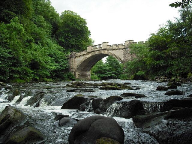 A stone bridge over a flowing river surrounded by lush greenery.