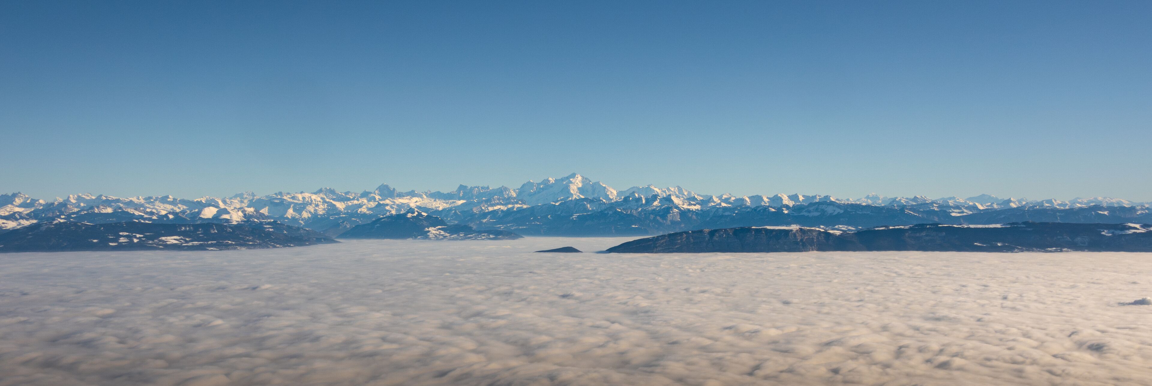 A mountain range with snow-capped peaks and a layer of clouds below.