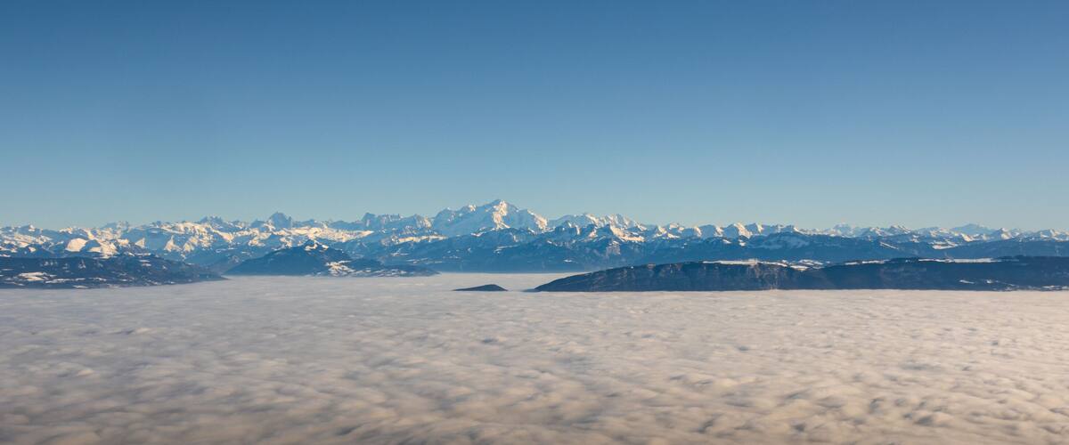 A mountain range with snow-capped peaks and a layer of clouds below.