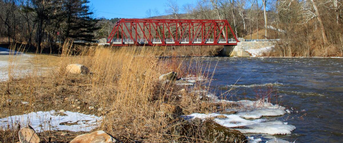 A red bridge over a river with snow patches and dry grass.