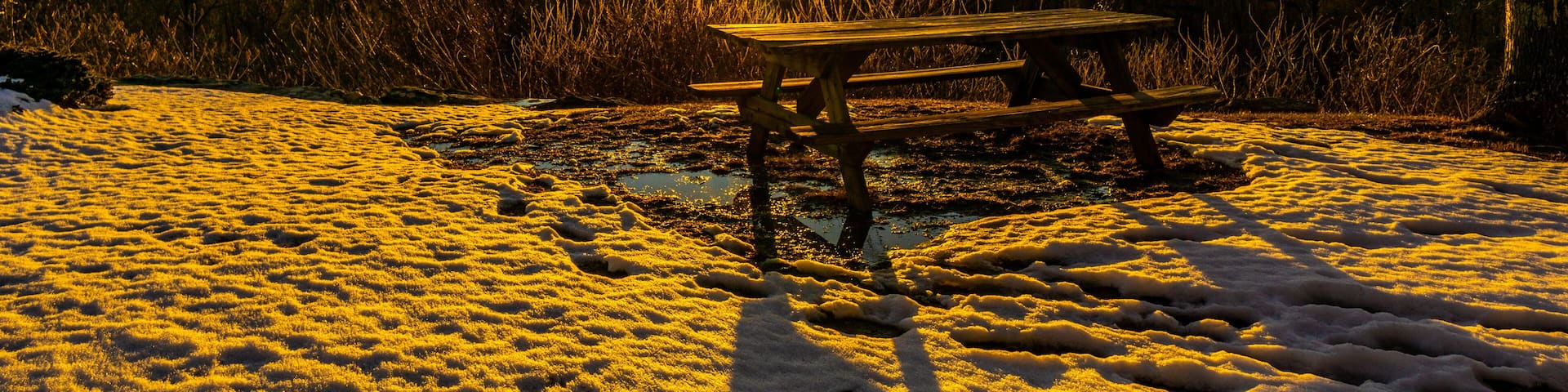 Granby Connecticut. A picnic table on a mountain top rests in snow and mud, while illuminated by a sunset view of another mountain scene. Beautiful sunset winter scene.