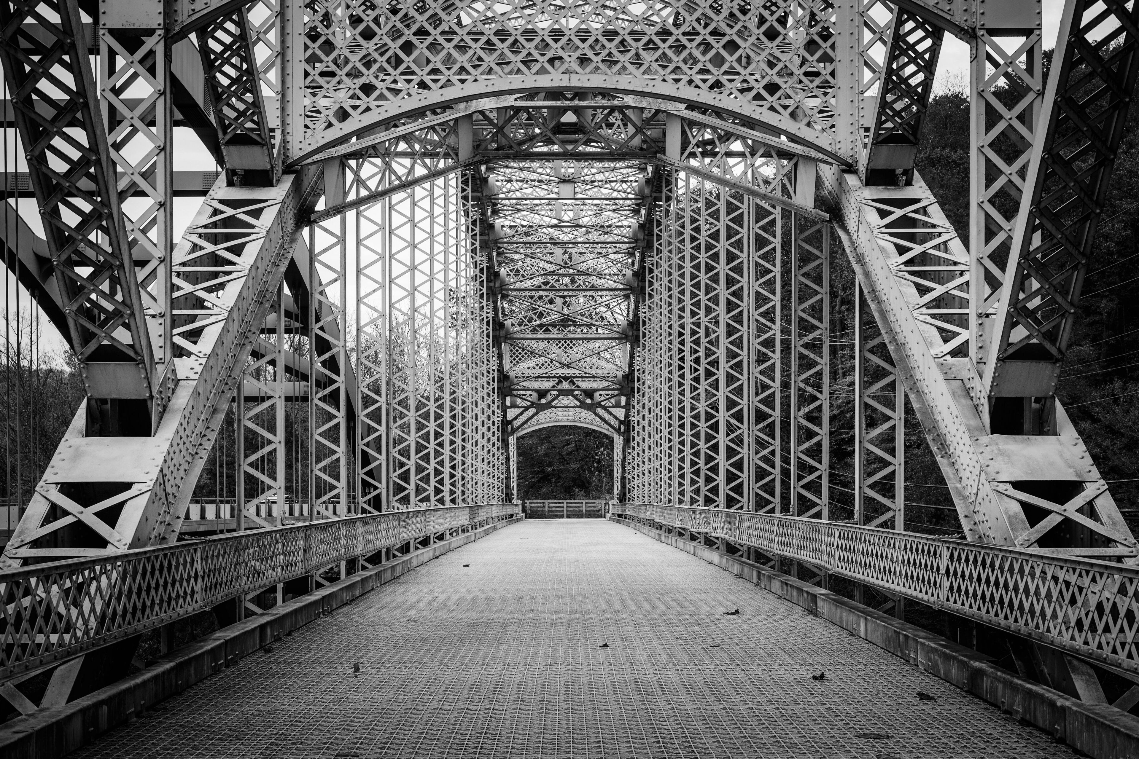 A black and white view of a steel bridge with a lattice structure and a pedestrian walkway.