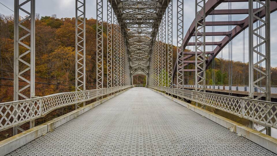 A metal bridge with a lattice structure and a paved walkway.
