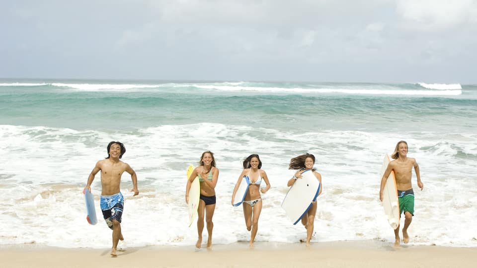 A beach with waves and people running with surfboards.