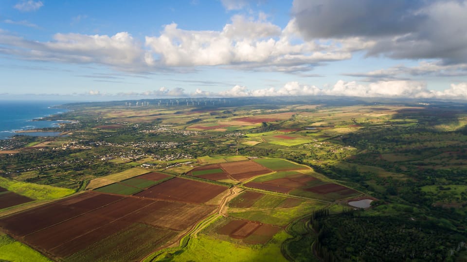 An aerial view of a coastal landscape with fields, a town, and wind turbines.