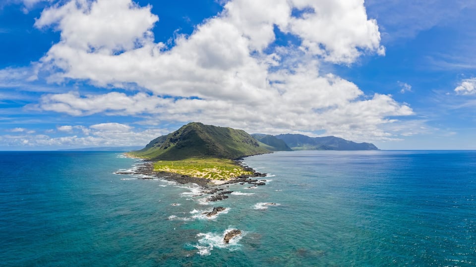 A clear blue sky, a large island with a mountain, and calm ocean waters.
