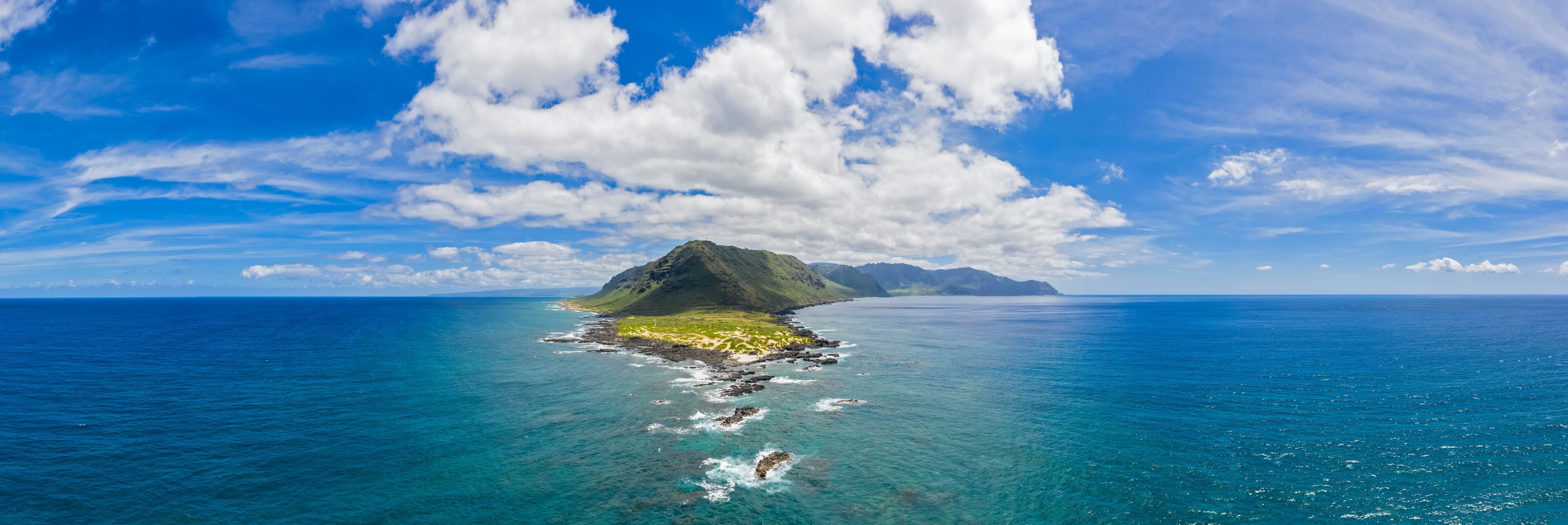 A clear blue sky, a large island with a mountain, and calm ocean waters.