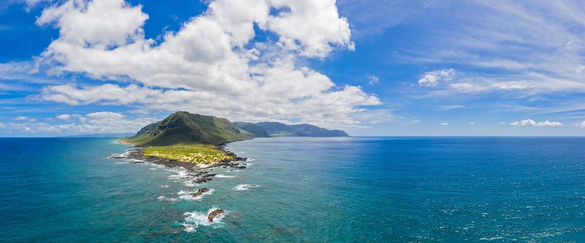 A clear blue sky, a large island with a mountain, and calm ocean waters.