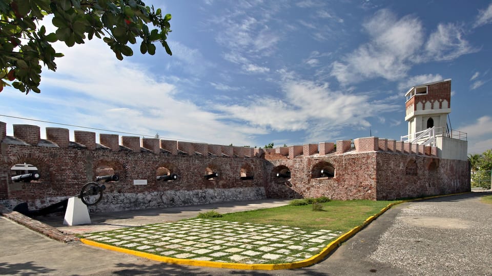 A historic brick fort with cannons, a watchtower, and a paved courtyard.