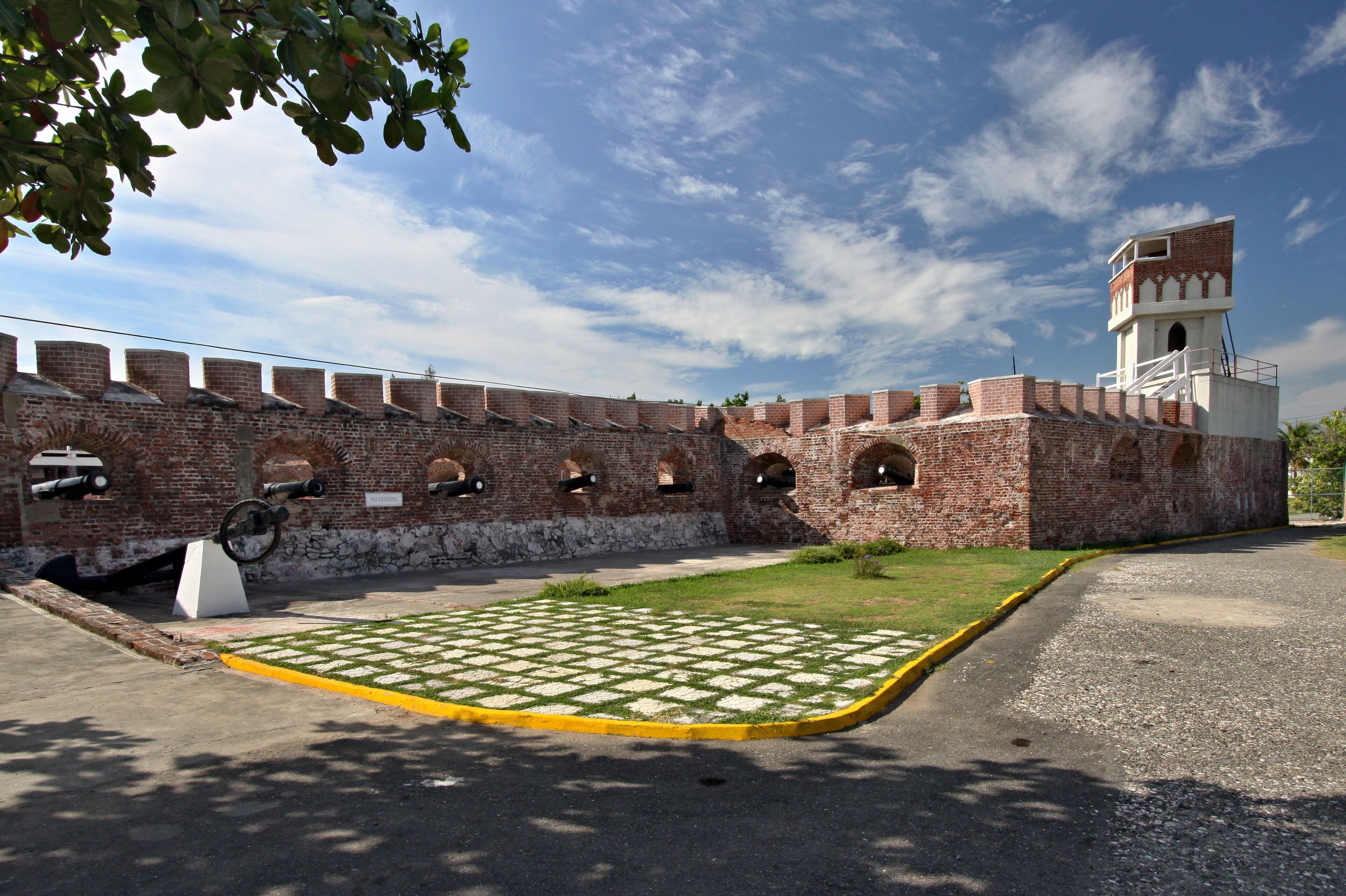 A historic brick fort with cannons, a watchtower, and a paved courtyard.