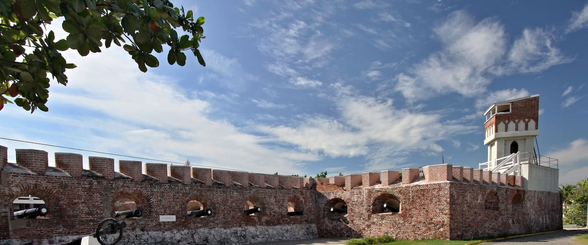 A historic brick fort with cannons, a watchtower, and a paved courtyard.