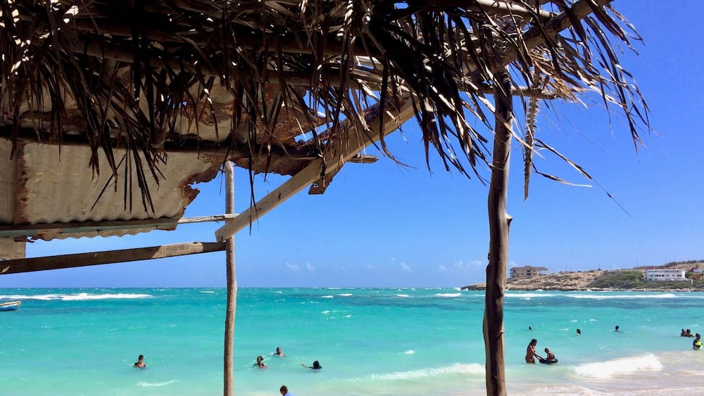 A beach with clear turquoise water, people swimming, and a wooden structure.
