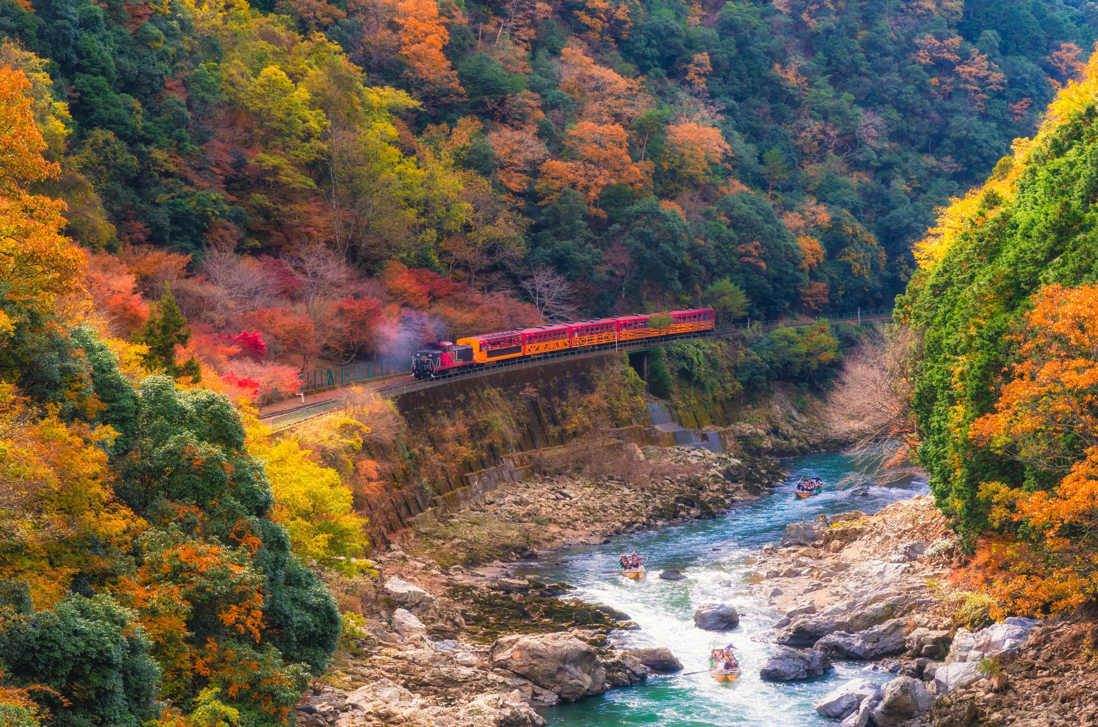 A train on a bridge over a river, surrounded by autumn-colored trees.
