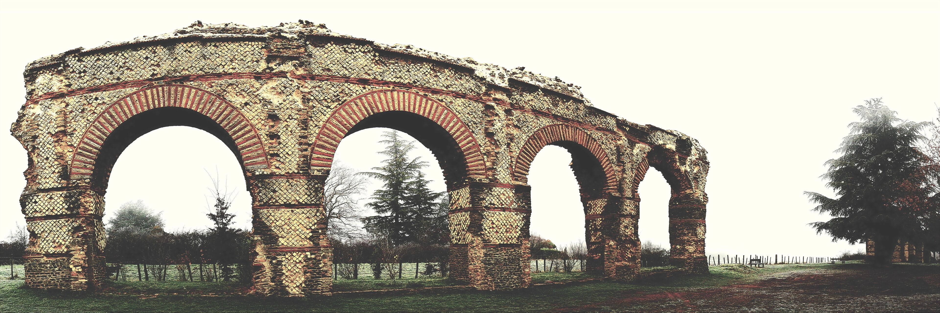 An ancient stone archway with intricate patterns, surrounded by trees and grassy areas.
