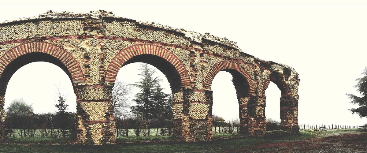 An ancient stone archway with intricate patterns, surrounded by trees and grassy areas.