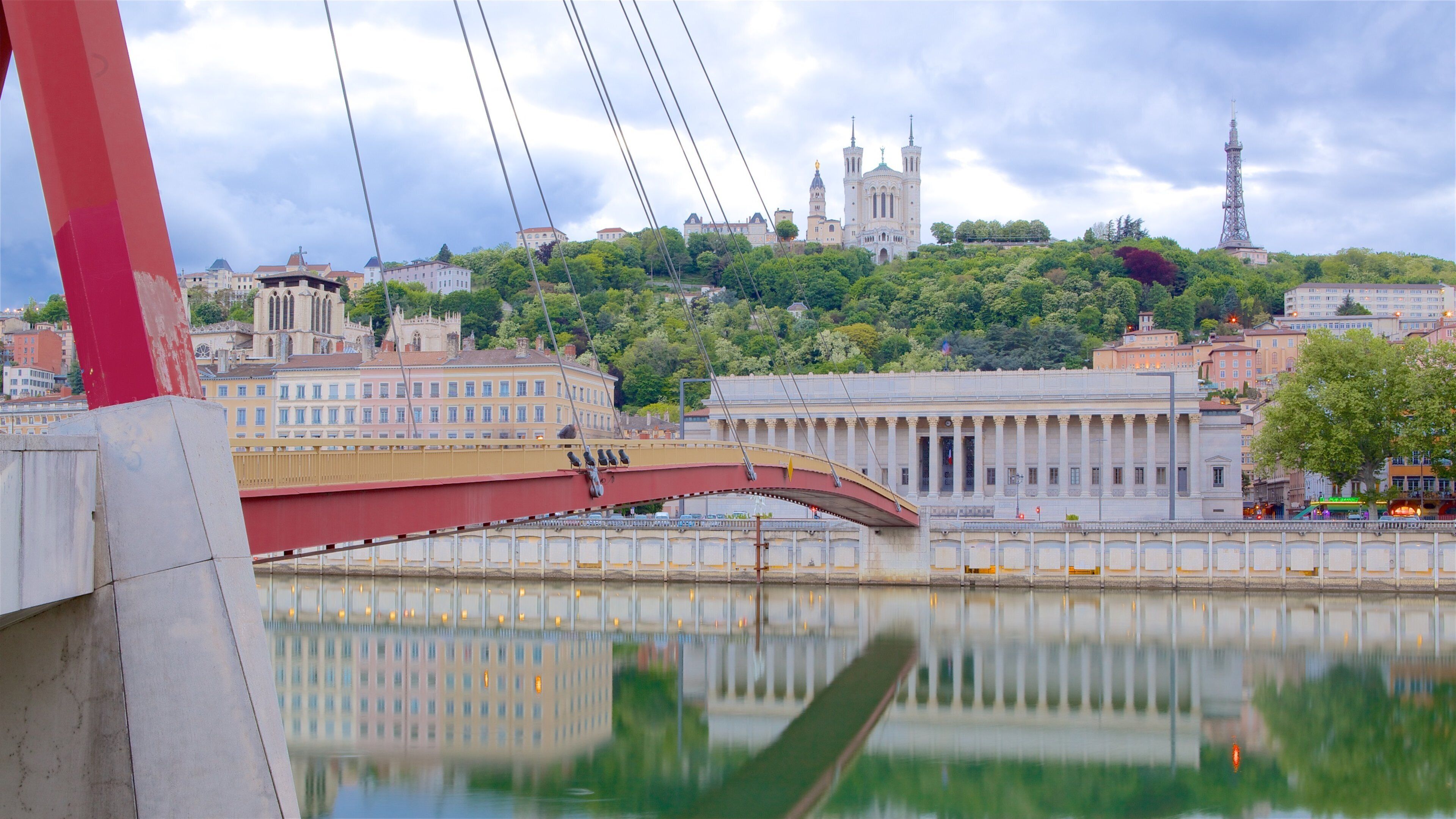 A river with a red bridge, a white building with columns, and a church with a tall tower in the background.