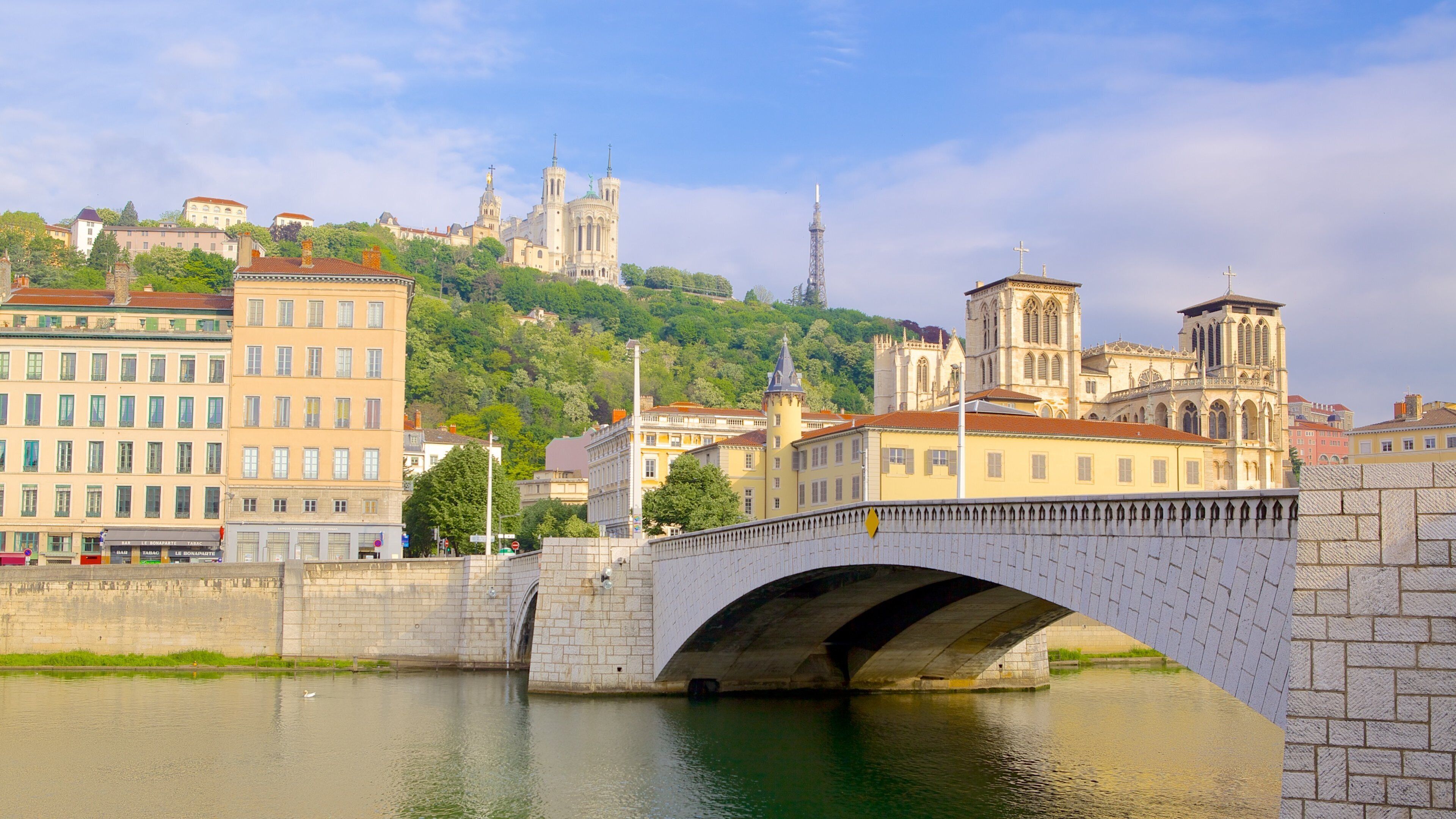 A stone bridge over a river, with buildings and a cathedral in the background.