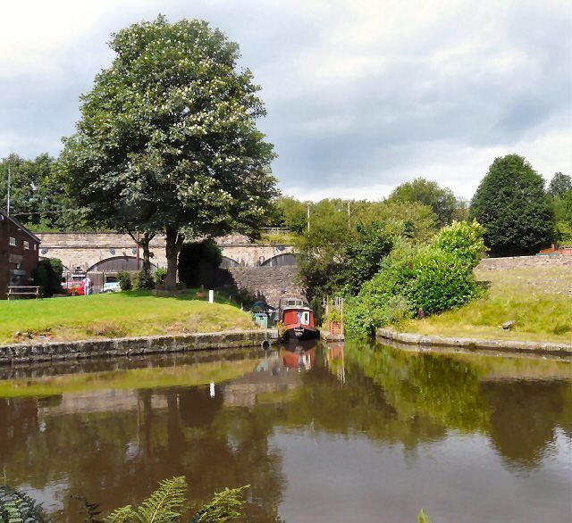 A canal with a red boat, a large tree, and a stone bridge in the background.