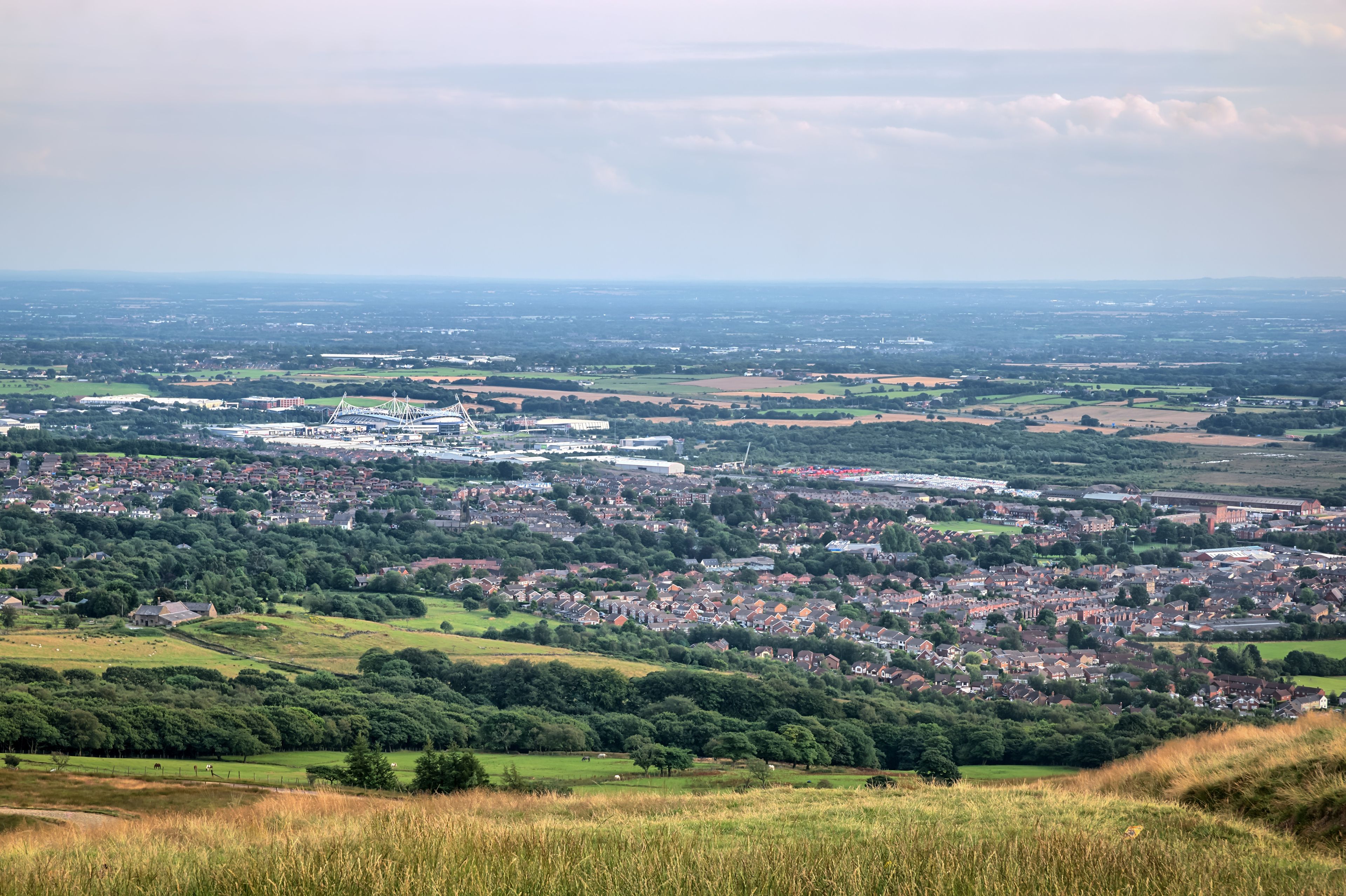 A panoramic view of a town with a mix of residential areas, green fields, and a large stadium.