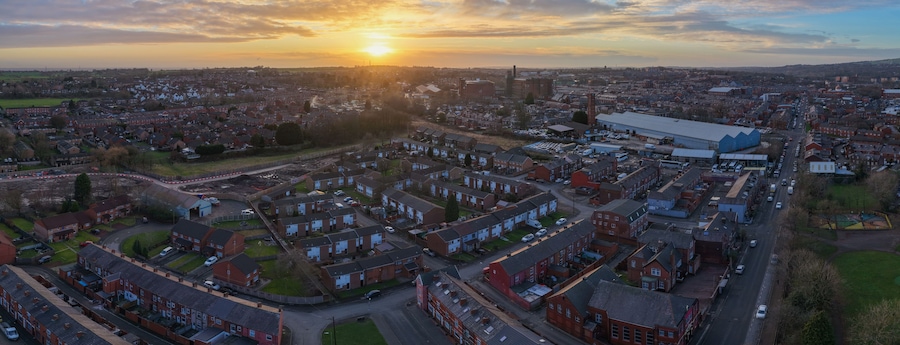 Una zona residencial con casas, un edificio industrial grande y una vista distante del sol poniéndose en el horizonte.