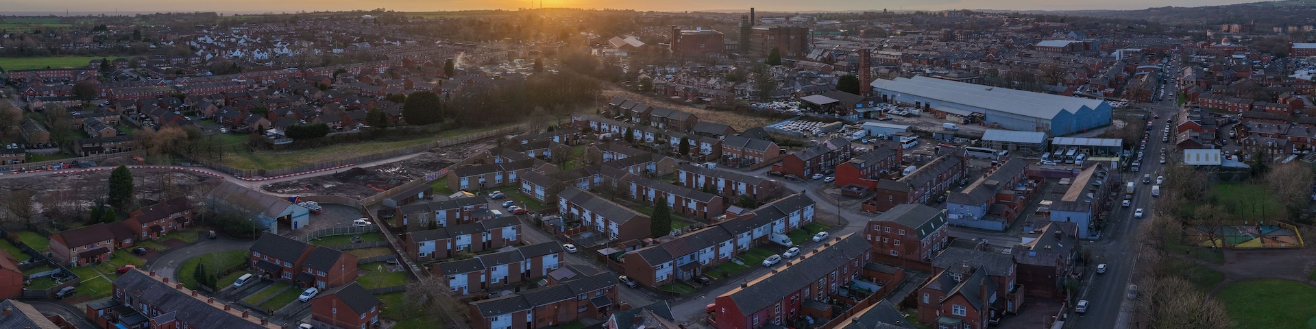 Una zona residencial con casas, un edificio industrial grande y una vista distante del sol poniéndose en el horizonte.