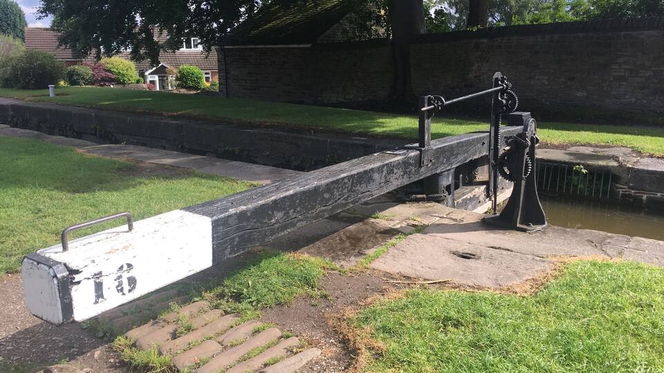 A lock gate with a chain mechanism, a grassy area, a brick wall, and trees in the background.