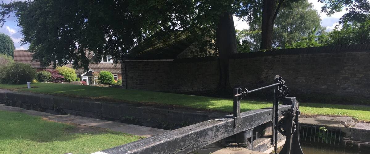 A lock gate with a chain mechanism, a grassy area, a brick wall, and trees in the background.