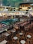 Un área de piscina en la azotea con varios niveles de asientos y zonas de comedor, rodeada de restaurantes y tiendas.