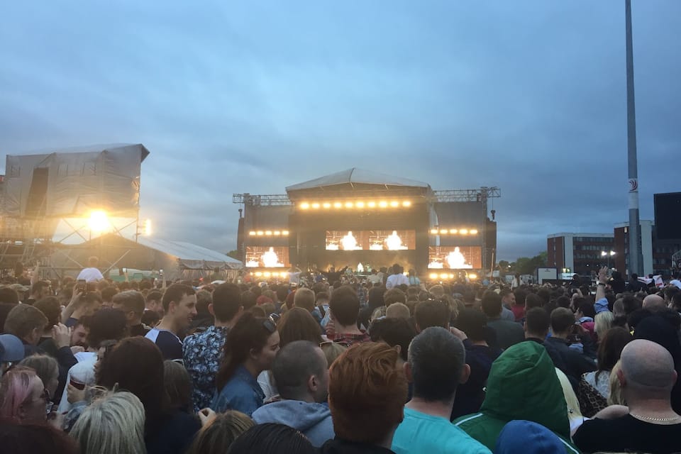 A large crowd gathered at an outdoor concert with a stage and lighting equipment.
