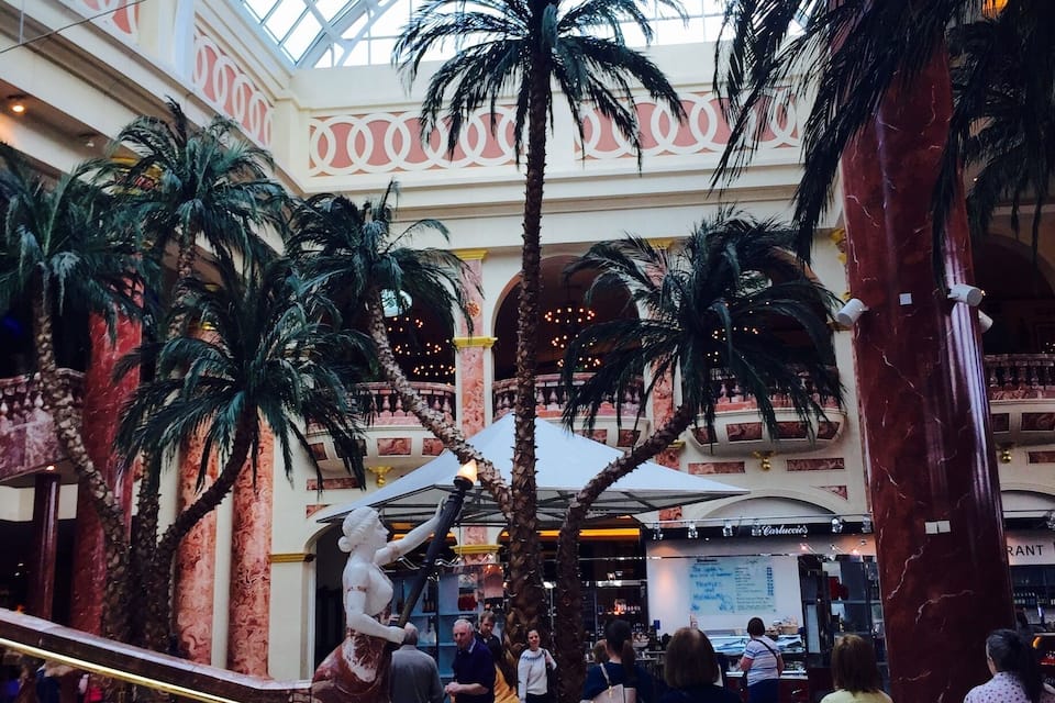 A shopping mall with a glass ceiling, palm trees, and a statue.