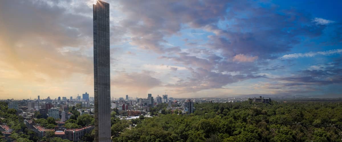 Aerial view of the slender Torre Reforma skyscraper with a sun flare overlooking the lush Chapultepec park and urban skyline under a cloudy sky in Mexico City, Mexico City, Mexico.