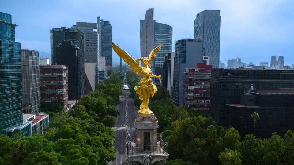 A golden statue in a park with a city skyline in the background.