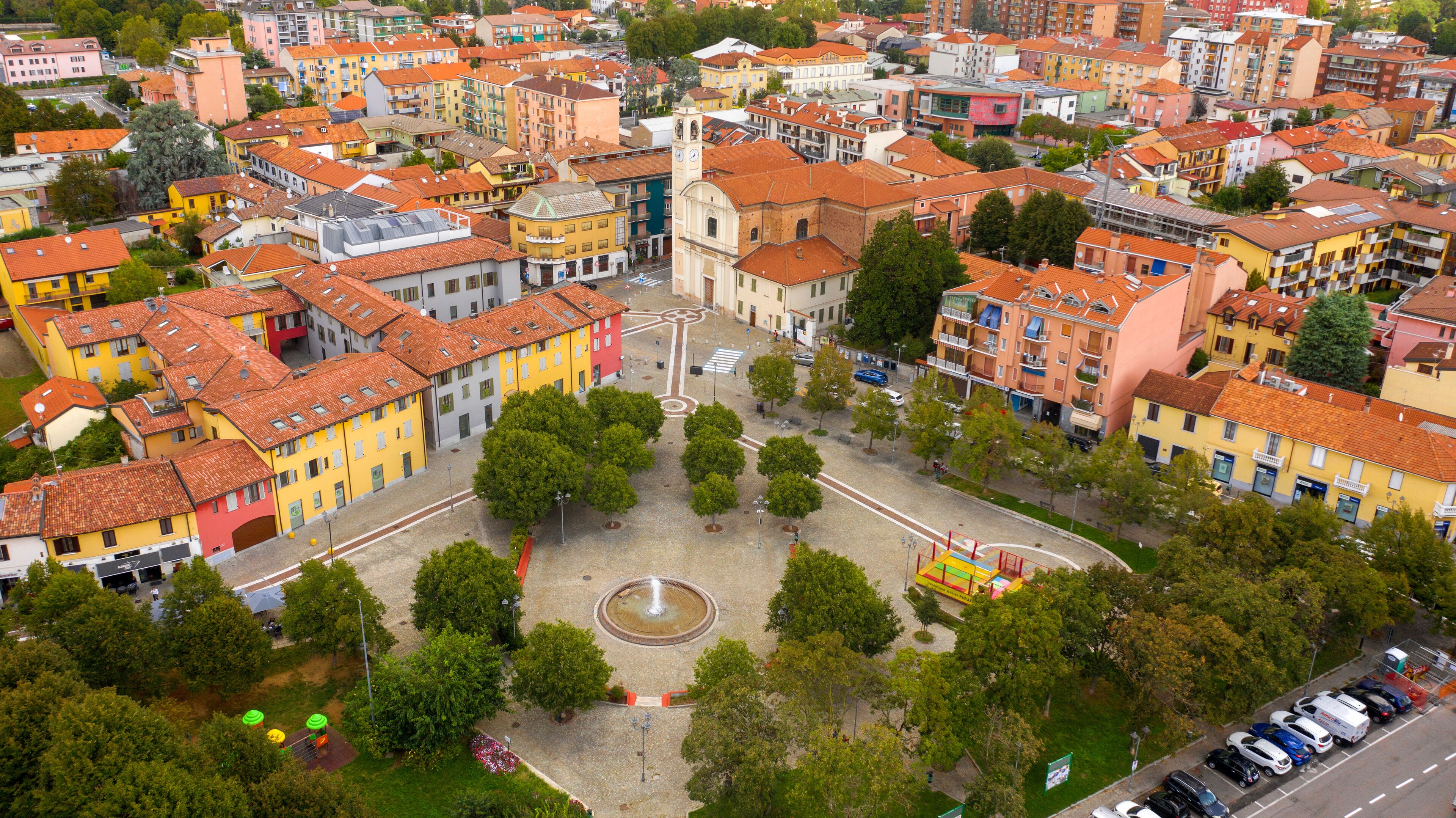 An aerial view of a colorful urban area with a central square, surrounded by multi-story buildings with red-tiled roofs.