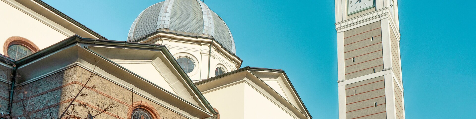 A church with a dome and a clock tower against a clear blue sky.