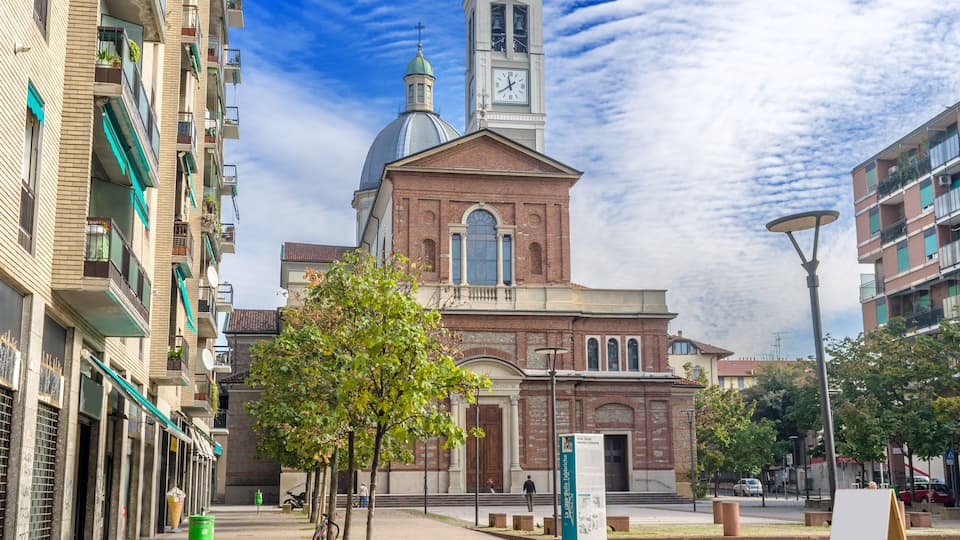 A historic church with a clock tower, surrounded by modern buildings and a clear sky.