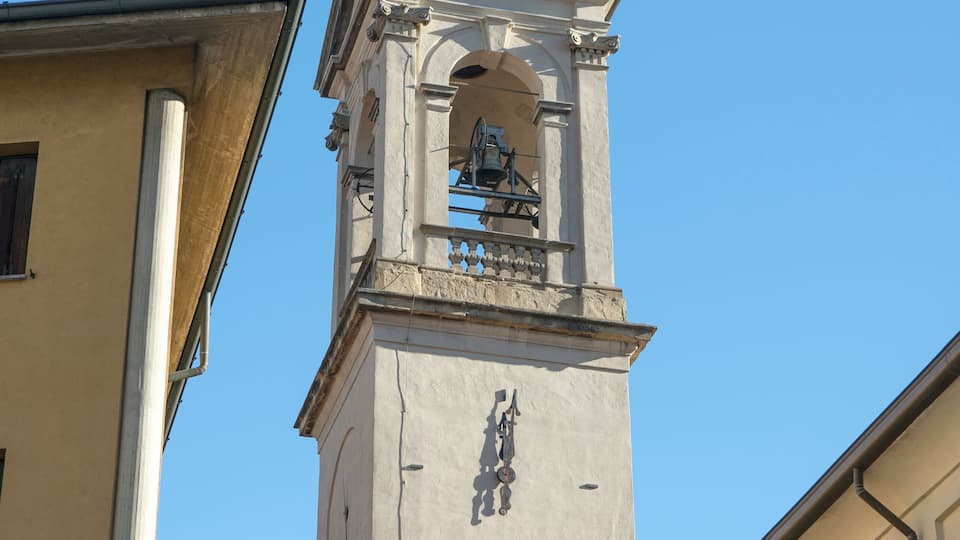 A tall clock tower with a weather vane on top, set against a clear blue sky.