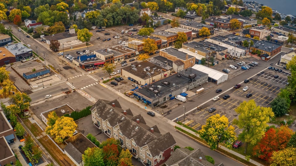 An aerial view of a town with a mix of residential and commercial buildings, a parking lot, and a waterfront.