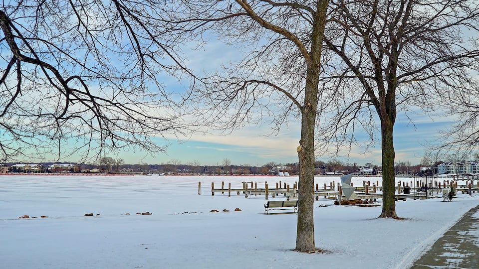 A snow-covered park with benches and trees.