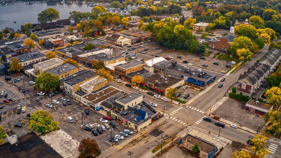 An aerial view of a town with a river, parking lots, and autumn-colored trees.