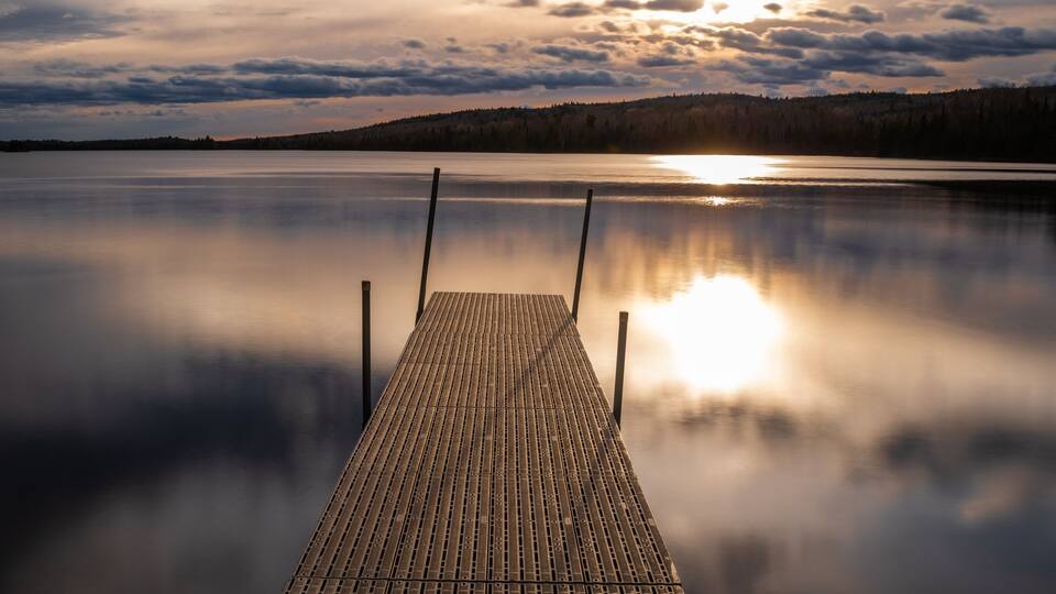 A wooden dock extending into a calm lake with a sunset in the background.